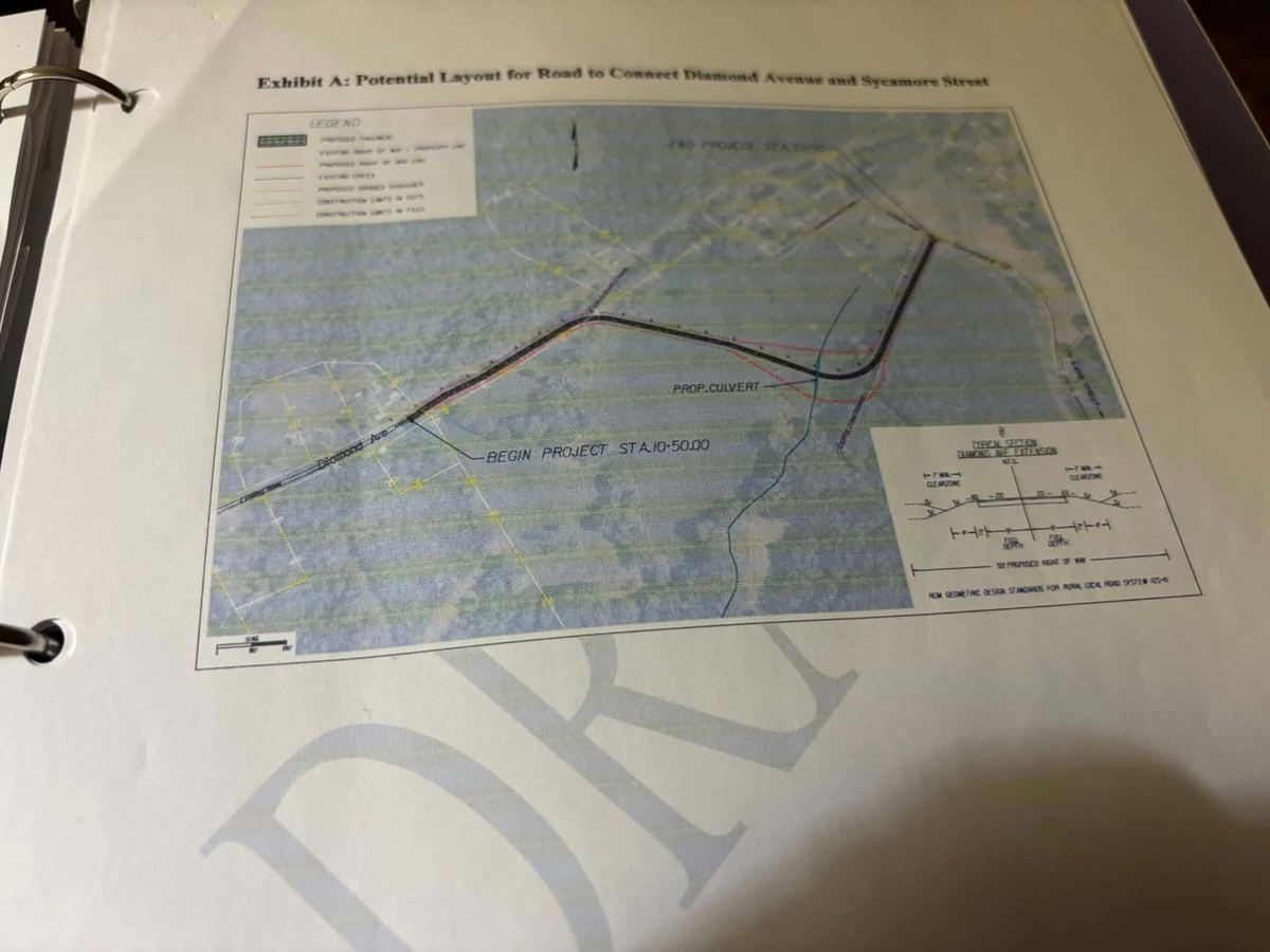 A page in a binder headed Exhibit A showing a drafted road alignment over an aerial map.